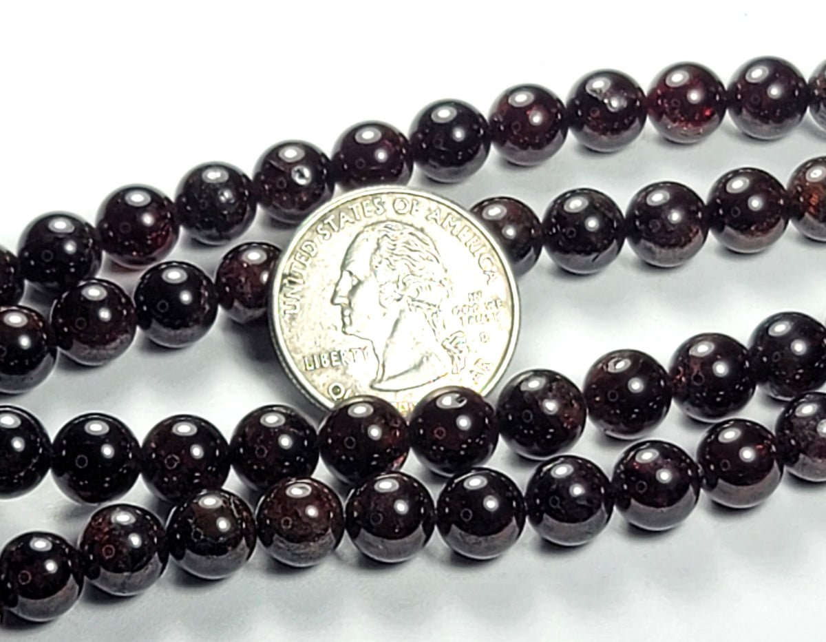 A strand of 8mm red garnet round gemstone beads with a coin for size comparison.