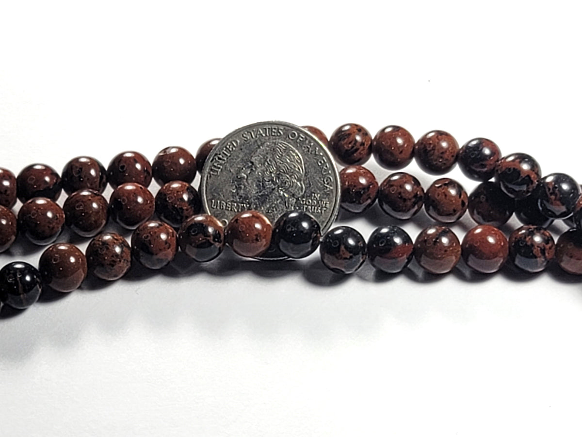A strand of round mahogany obsidian gemstone beads, with beads displaying a natural brown color and a US quarter for scale reference.