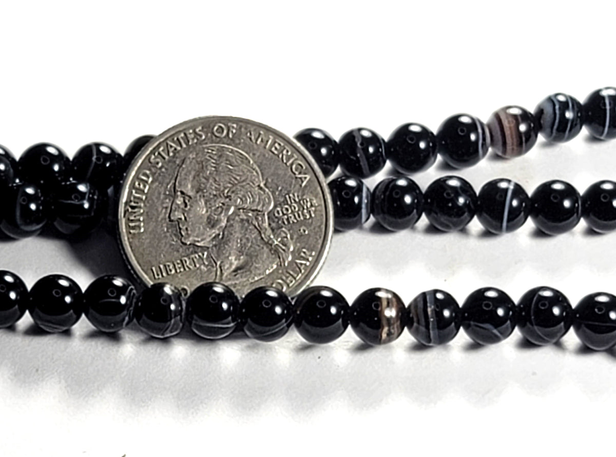 A strand of black sardonyx round gemstone beads, with a coin for size comparison.