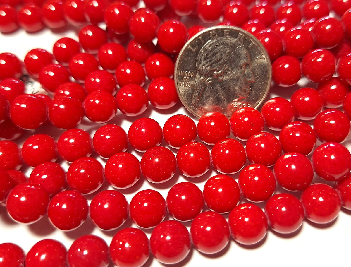 A close-up of red jade dyed round gemstone beads with a coin for scale.