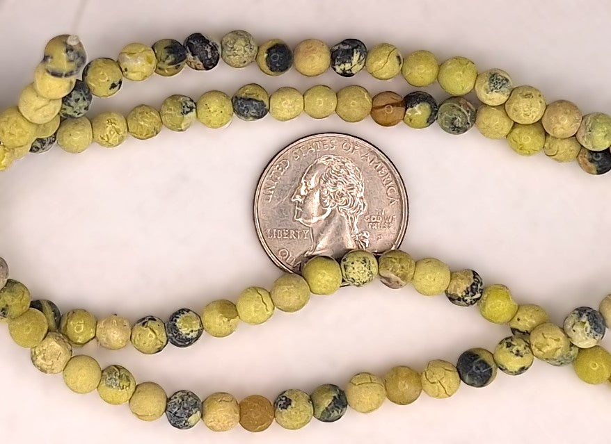 A strand of round, mottled yellow-green and black beads, shown with a US quarter coin in the center for scale, on a plain off-white background.
