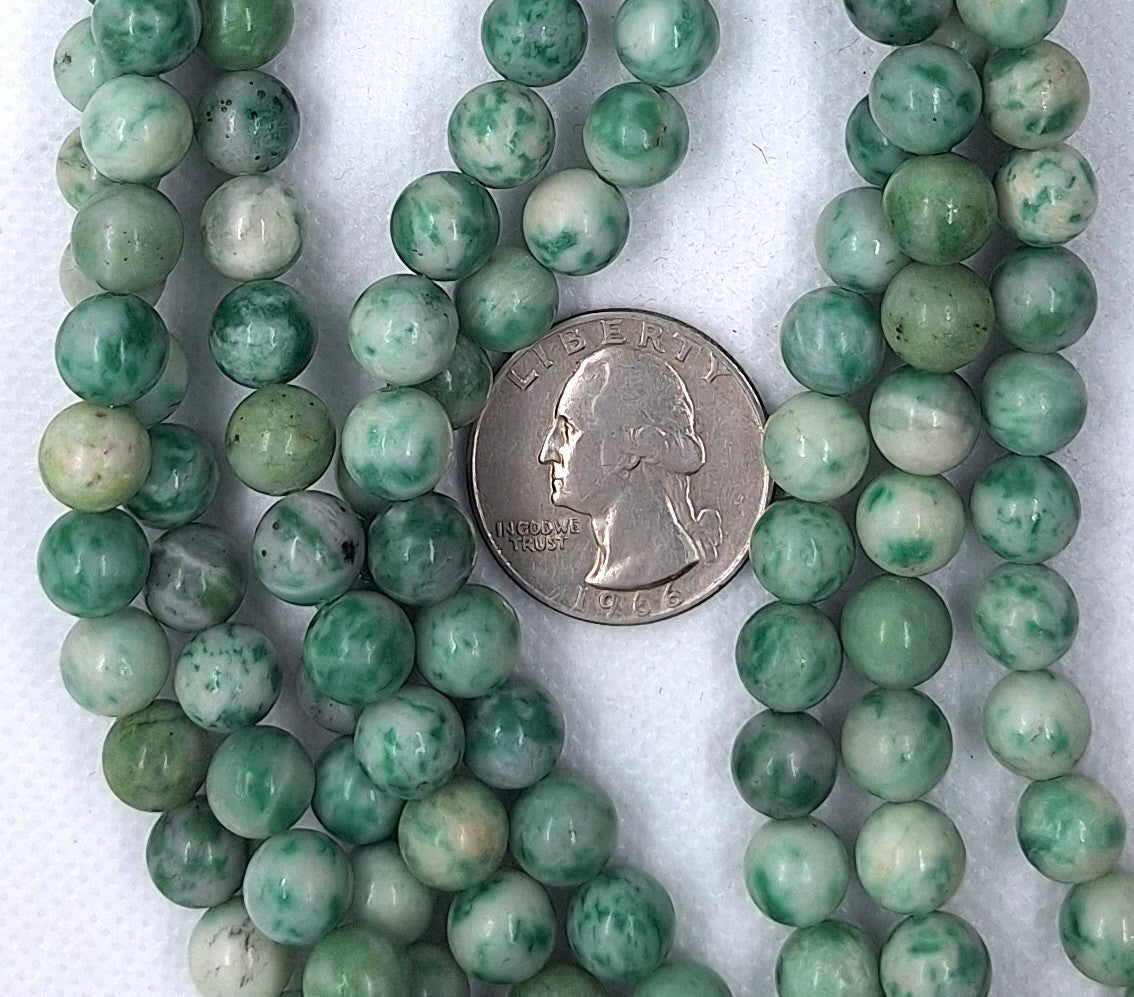Strands of green beads with a quarter for size comparison on a white background