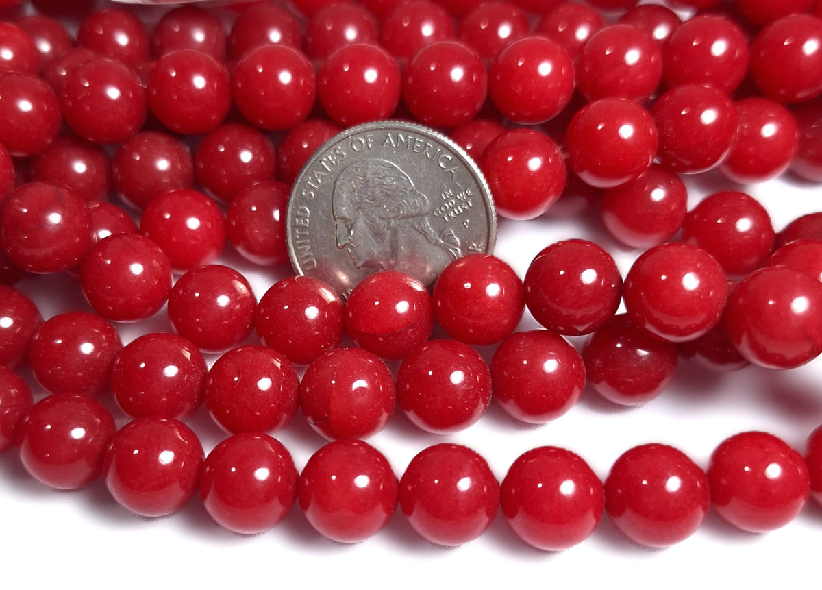 A close-up of red jade dyed round gemstone beads with a quarter for scale.
