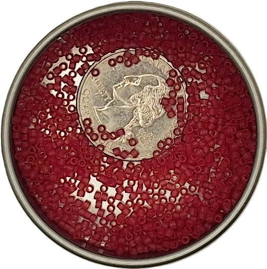 Red seed beads filling a round metal tin, with a silver coin placed on top as a size reference, against a white background.