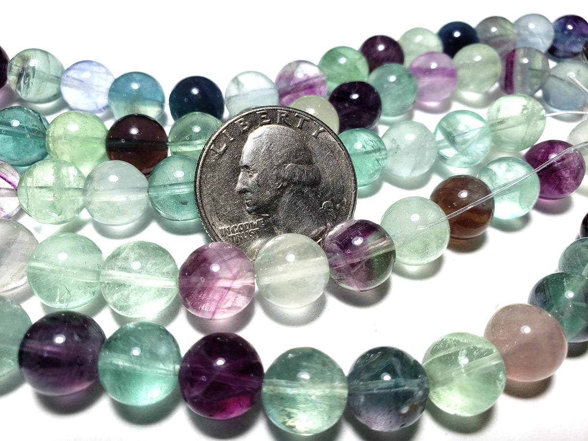 A strand of multicolored round fluorite beads with a US quarter for size comparison.