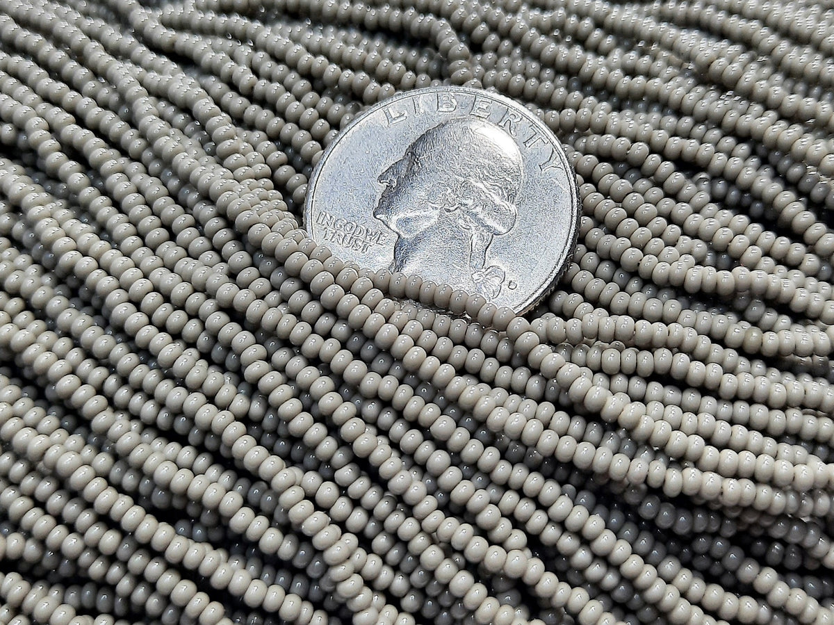 A close-up of opaque gray Czech seed beads with a coin for size comparison.