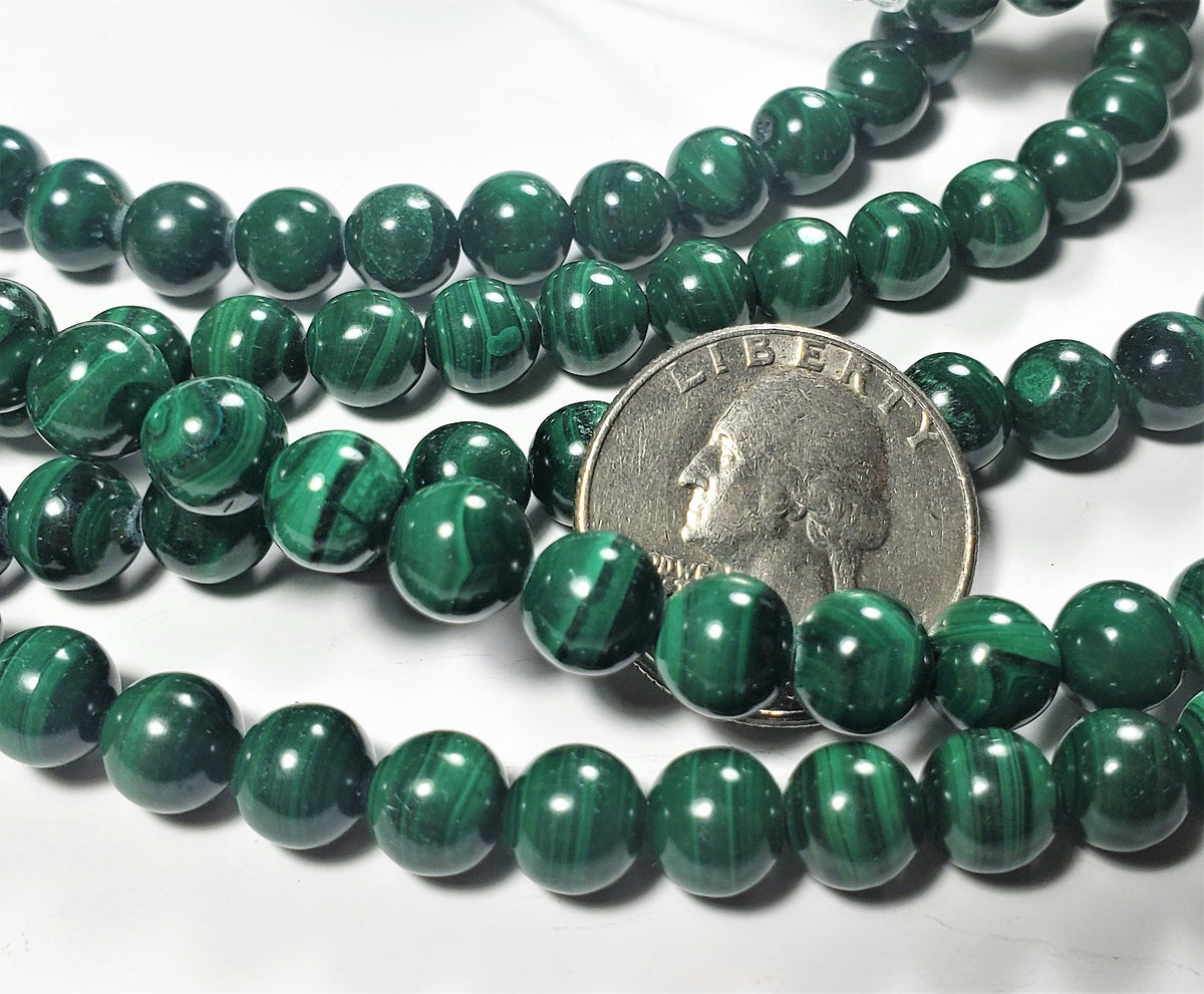 A strand of 8mm round malachite gemstone beads with a green color, laid out on a surface with a coin for size comparison.