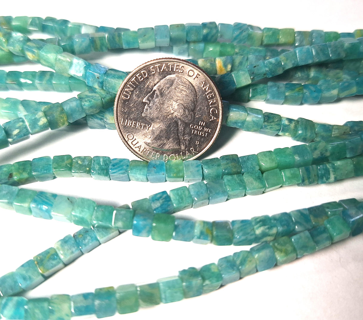 Blue-green Russian amazonite square cube beads with a quarter for size comparison on a white background