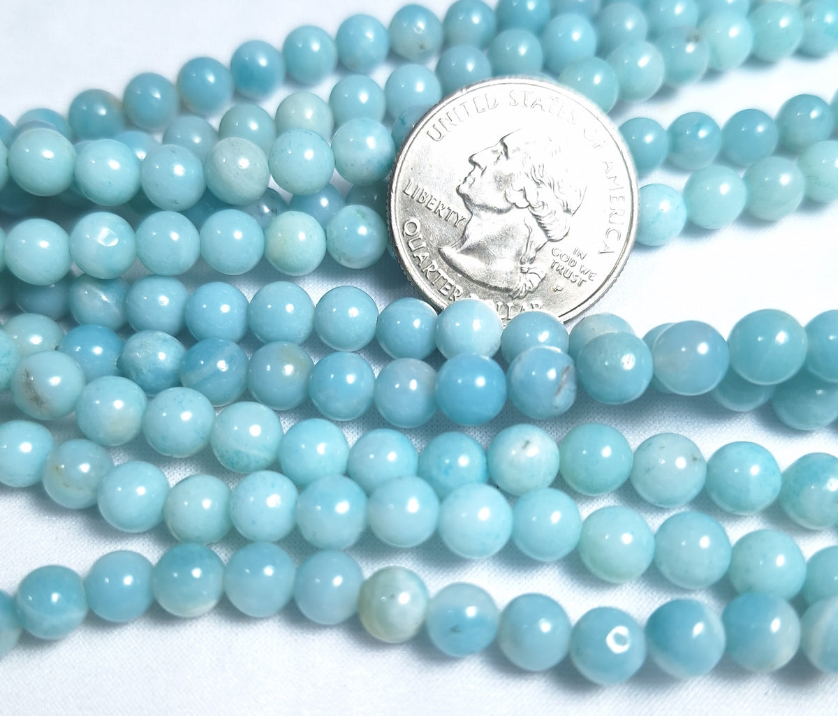 A series of round, blue Amazonite gemstone beads laid out alongside a quarter for scale.