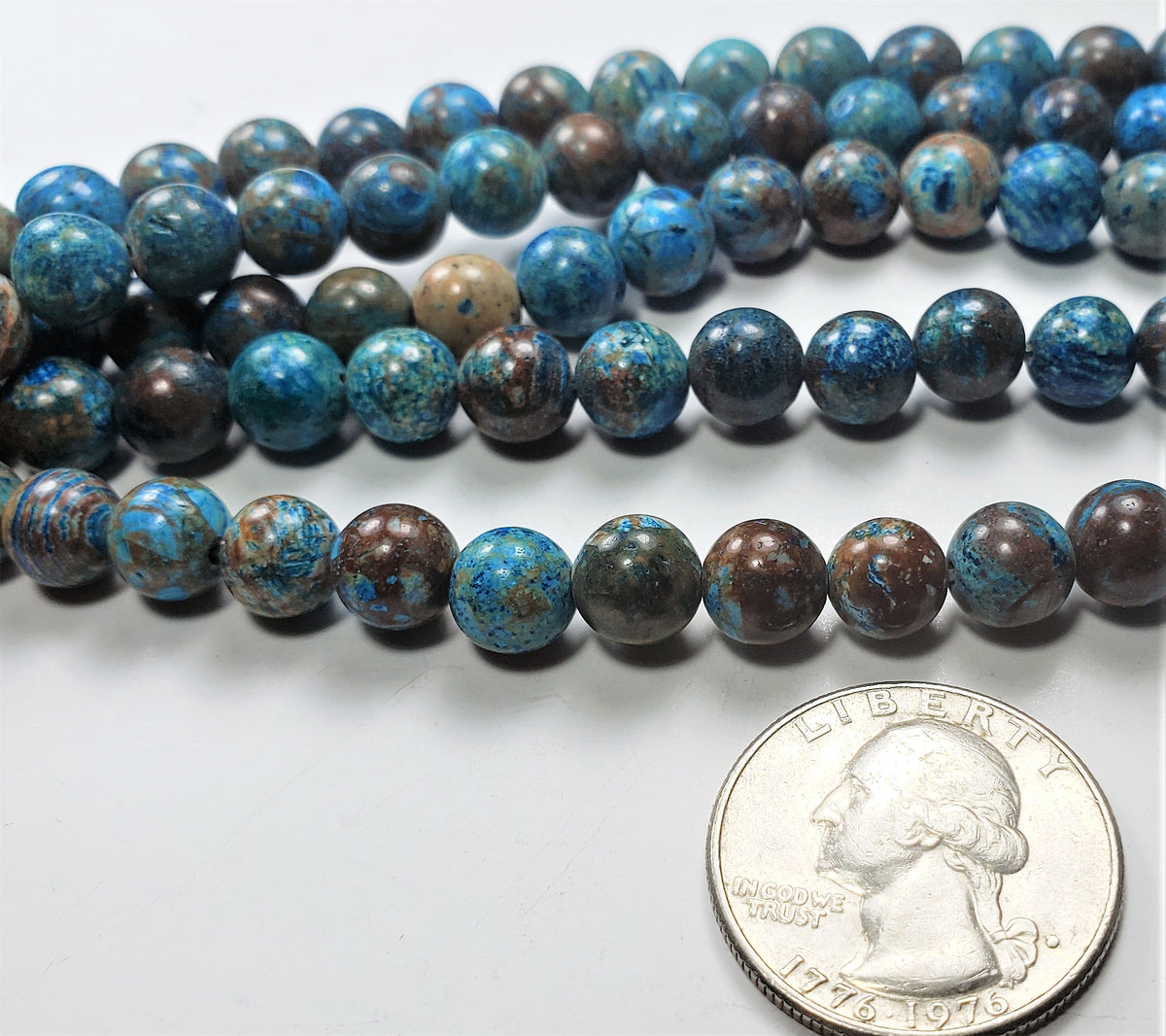 A strand of 8mm round blue imperial jasper gemstone beads laid out next to a coin for size comparison.
