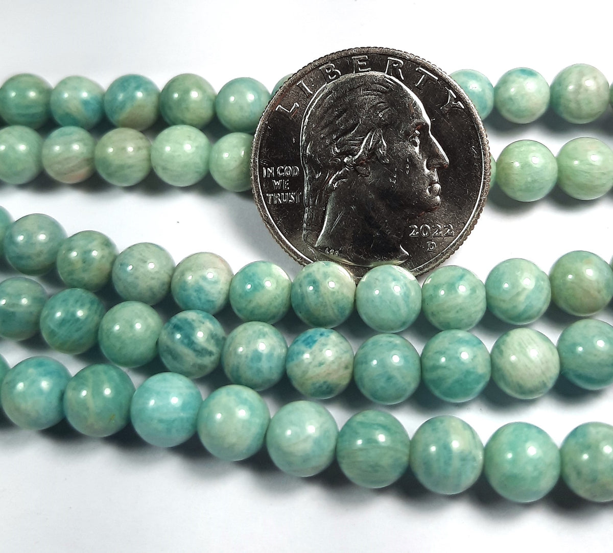 A strand of round Russian amazonite beads with a coin for size comparison.